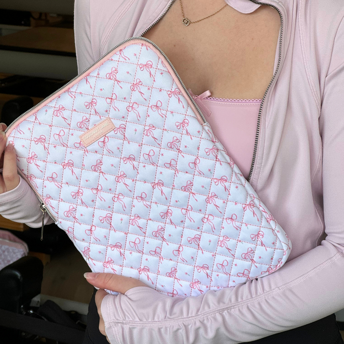 Person in pink top holding a quilted iPad sleeve with a dainty bows pattern and zip closure.