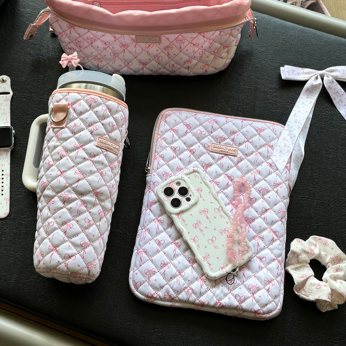 Pink and white quilted iPad sleeve with dainty bow pattern and matching accessories on a black table.