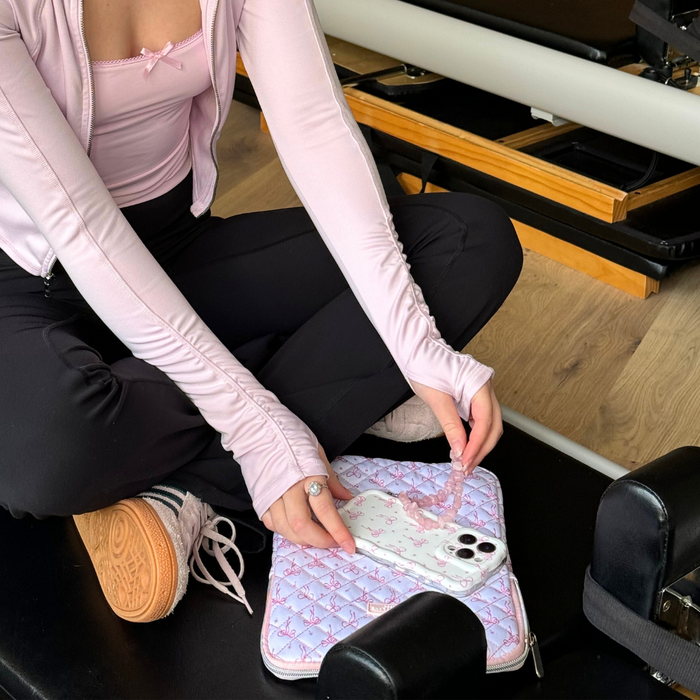 Quilted Dainty Bows iPad sleeve by Coconut Lane rests on gym equipment beside woman in a pink top holding a phone.