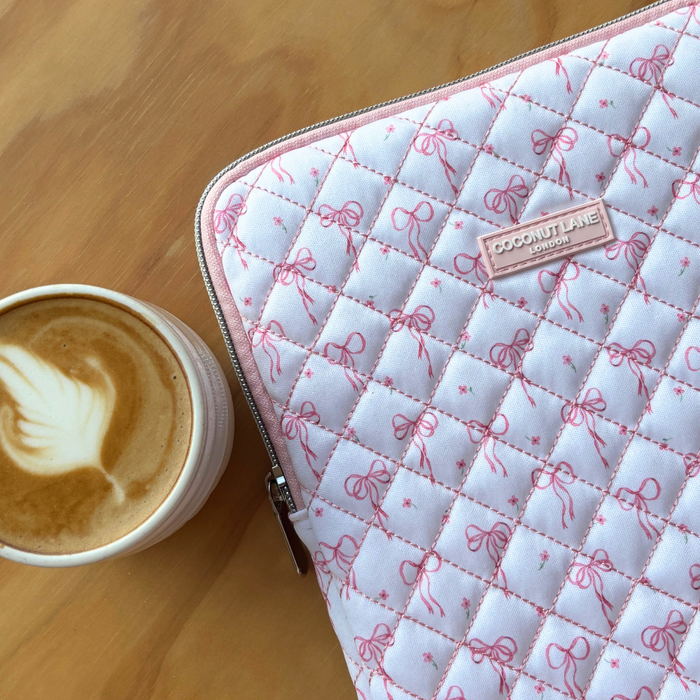 Quilted iPad sleeve with dainty bow pattern beside a cup of latte on a wooden table.
