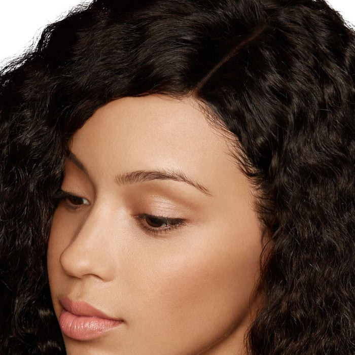 A serene woman with smooth skin and long, curly black hair gazes downward, her calm expression highlighted by soft curls.