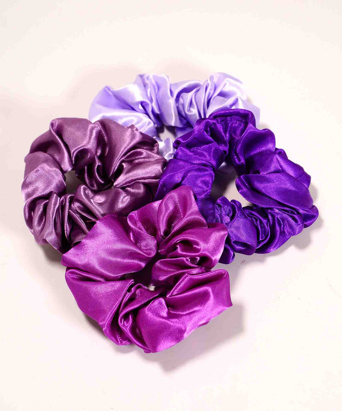 Four satin scrunchies in lavender, lilac, deep violet, and magenta cluster on a light surface, adding style to any collection.