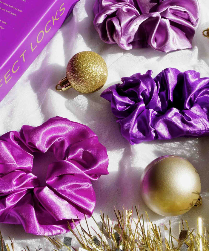 Purple and gold satin scrunchies with glittery gold ornaments on a white surface, next to a purple PERFECT LOCKS box in the corner.