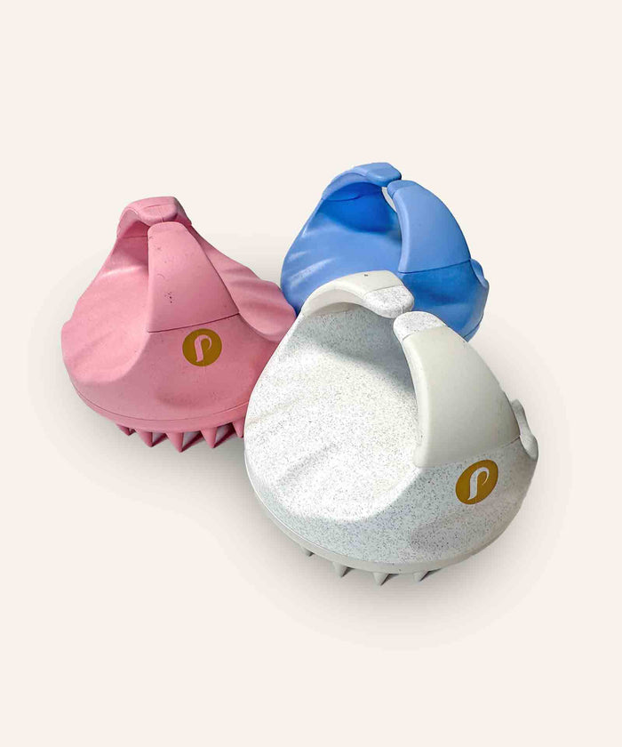 Three silicone scalp massagers in pink, blue, and off-white with rounded handles and short bristles for a gentle massage experience.