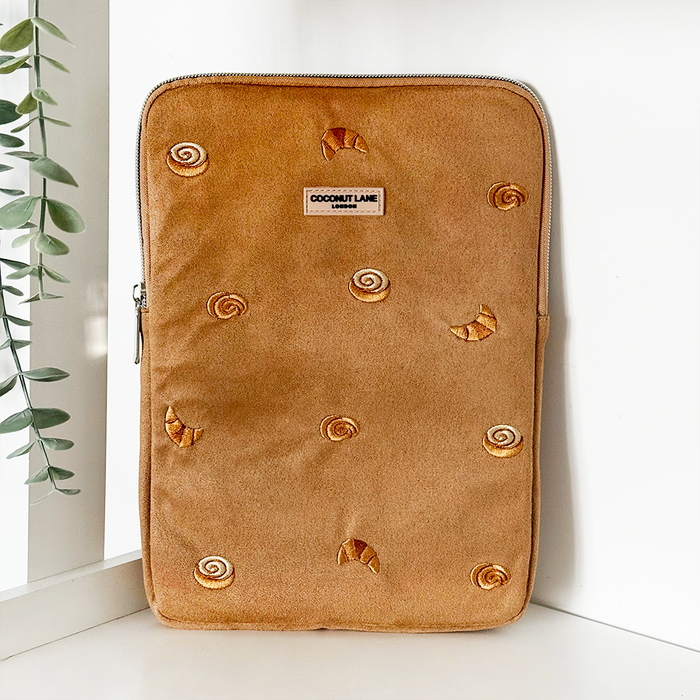 Tan suedette iPad sleeve with pastry pattern, standing upright near a wall and a green plant.