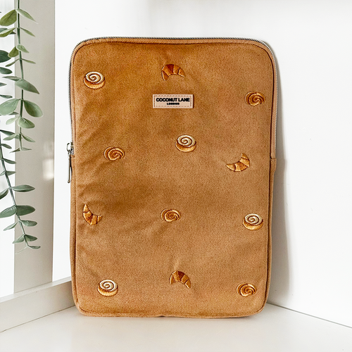 Tan suedette iPad sleeve with pastry pattern, standing upright near a wall and a green plant.