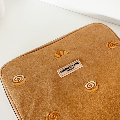 Tan suedette iPad sleeve with embroidered pastries and a Coconut Lane logo label at the center.