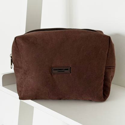 Chocolate brown suedette makeup bag with Coconut Lane branding, shown on a white shelf.