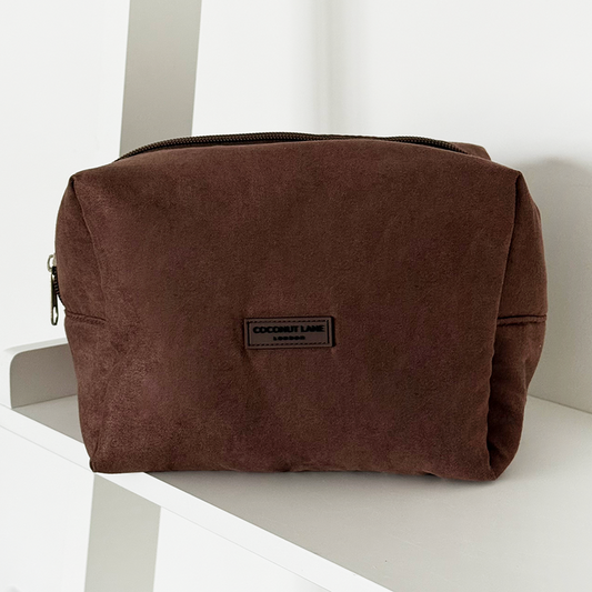 Chocolate brown suedette makeup bag with Coconut Lane branding, shown on a white shelf.
