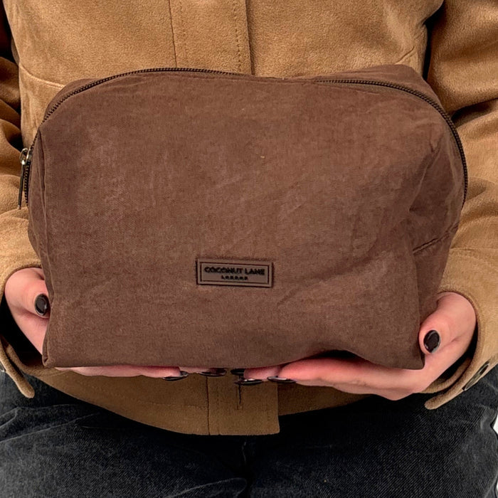 Chocolate brown Coconut Lane suedette makeup bag held by person in a tan jacket and dark pants.