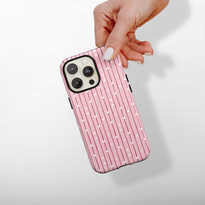 Phone case with pink and white striped and heart pattern held by a hand on a light background