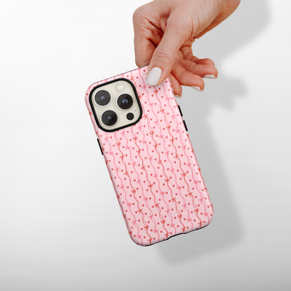 Phone case with a pink bows and hearts pattern held by a hand on a light gray background