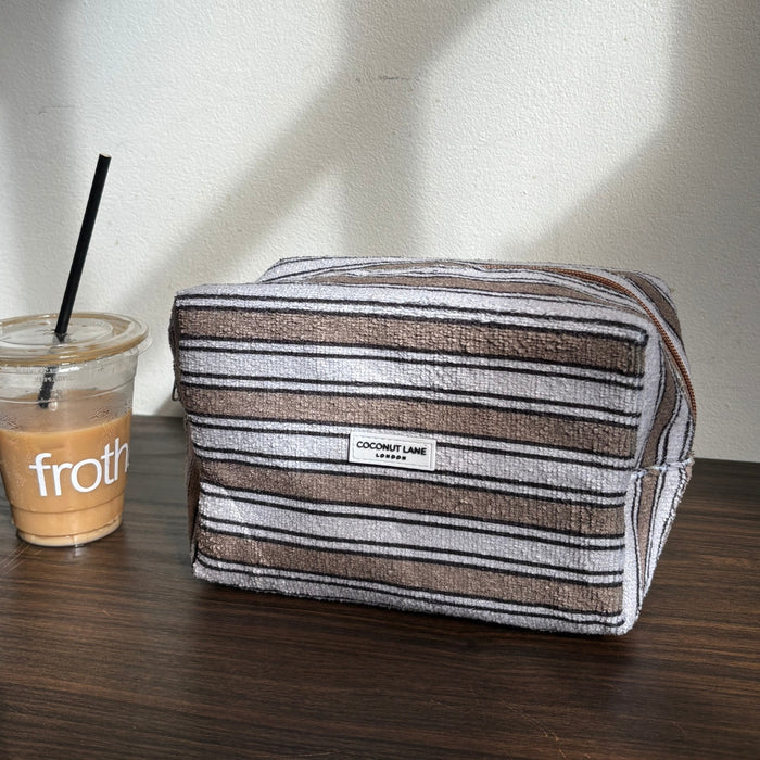 Coconut Lane makeup bag with retro stripes on a dark wooden table beside an iced coffee.