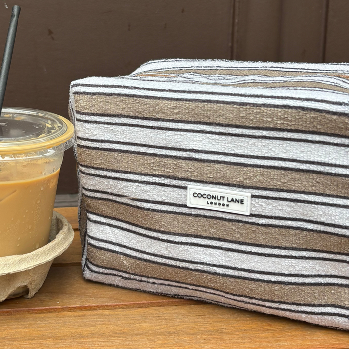 Iced coffee next to a Coconut Lane makeup bag with retro stripes, both on a wooden surface.
