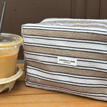 Iced coffee next to a Coconut Lane makeup bag with retro stripes, both on a wooden surface.