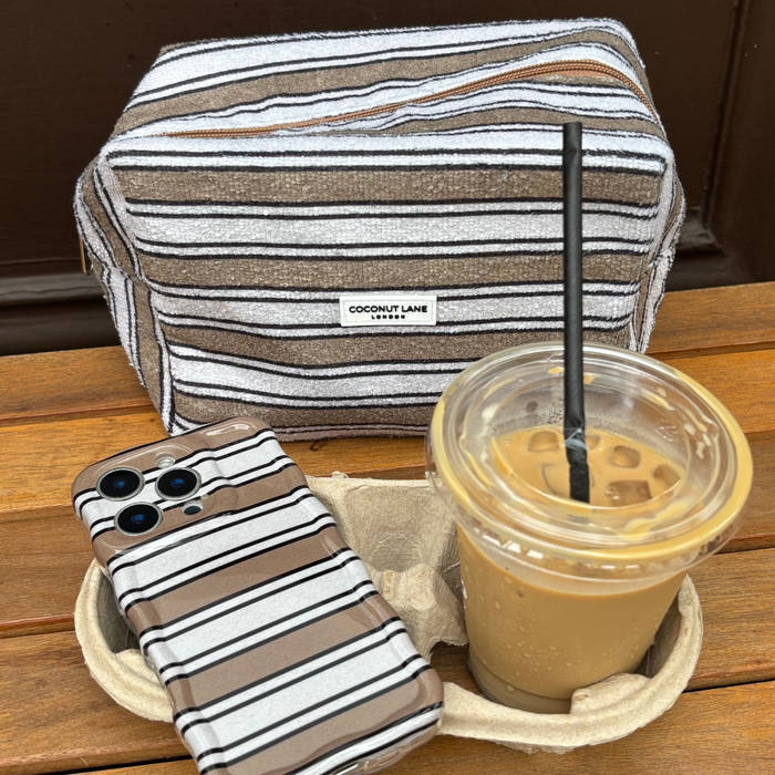 Coconut Lane towel makeup bag with retro stripes, matching striped phone case, and iced coffee on a wooden surface.