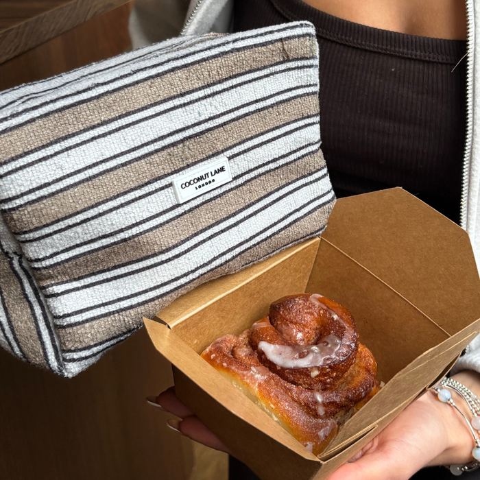Coconut Lane Towel Makeup Bag with retro stripes held next to an open box containing a glazed cinnamon roll.