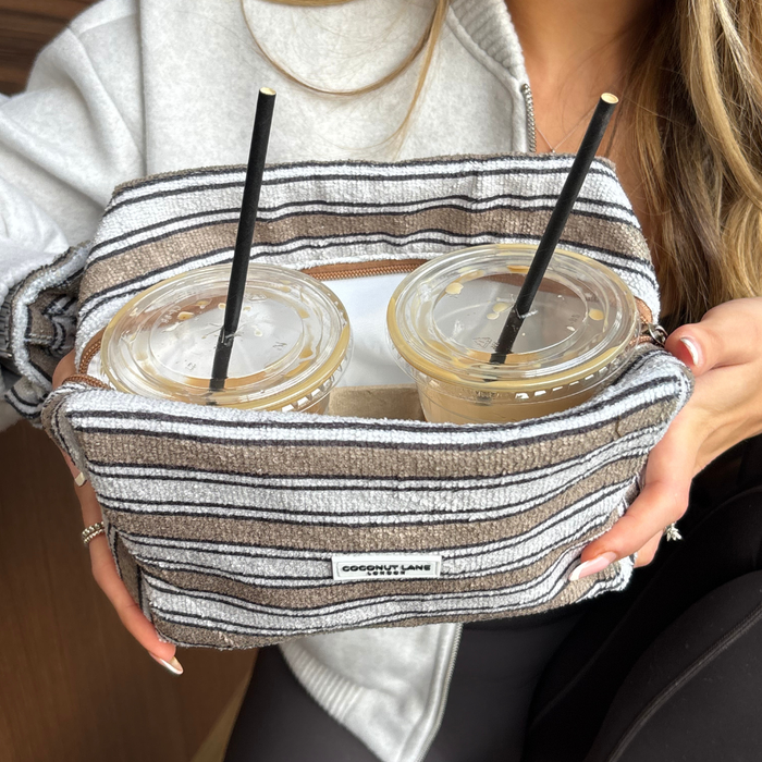 Two iced coffees with straws held in a Coconut Lane towel makeup bag featuring retro stripes.