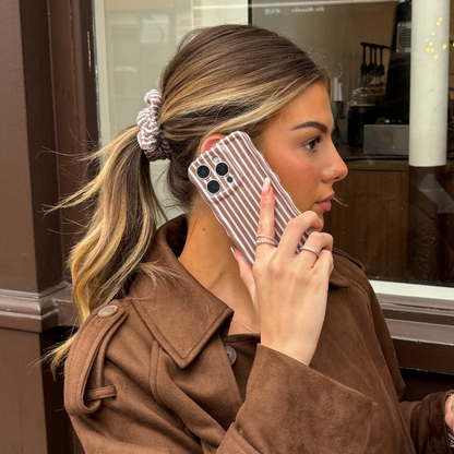 Woman with highlighted hair in a ponytail wears a chestnut striped towel scrunchie and holds a matching striped phone case.