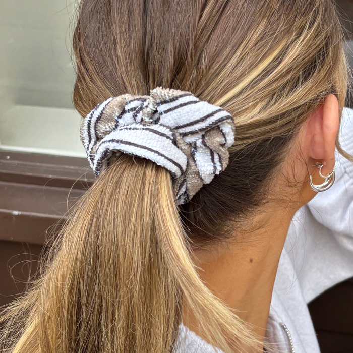 Woman with a low ponytail wears a striped Coconut Lane towel scrunchie and silver hoop earrings.