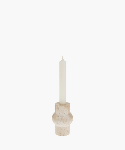 A tall white candle in a rounded, beige travertine stone holder with a textured surface. The minimalist design evokes a calm and serene atmosphere. | SW Home
