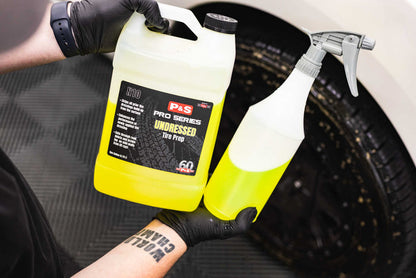 A Jug and spray bottle of P&S Undressed held by a person with gloves against a car tire background.