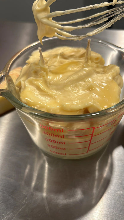 Creamy whipped body butter in a glass measuring cup on a stainless countertop