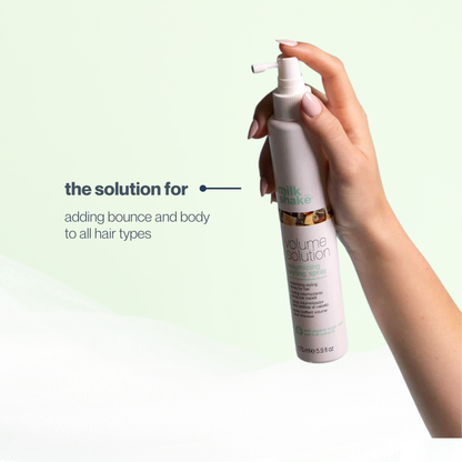 Hand holding a bottle of milk_shake  'Volume Evolution' hair product with text on a light green background