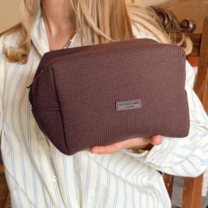 Coconut Lane chocolate brown waffle-textured makeup bag held by a person in a striped shirt.